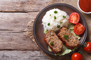 pieces of meat loaf and rice, vegetables on a plate top view
