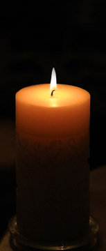 Unusual long view of large lit candle in darkness.