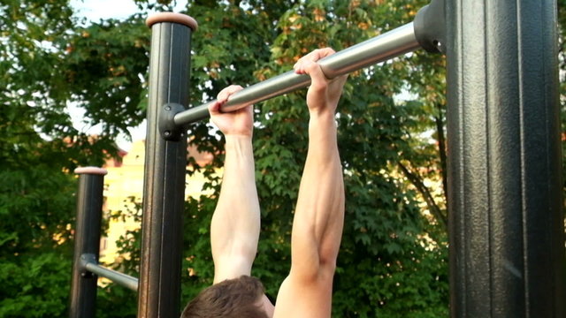 Young Muscular Man Doing Pull Ups On A Bar In Park