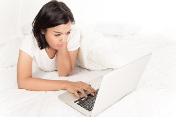 Smiling woman using a laptop while lying on her bed