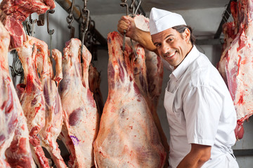 Butcher Standing By Meat Hanging In Slaughterhouse
