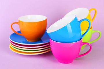 Colorful cups and saucers on color background