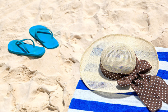 Straw hat, towel and flip flops on  sand beach
