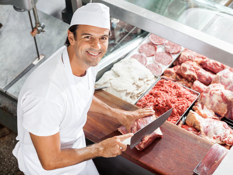Smiling Butcher Cutting Meat At Counter