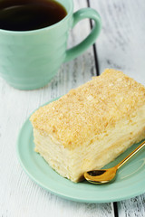 Napoleon cake on plate and cup of tea on table close-up