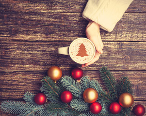 Fototapeta na wymiar Female holding cup of coffee with cream christmas tree on a tabl