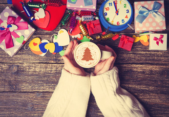 Female holding cup of coffee with cream christmas tree on a tabl