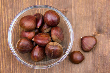 Glass bowl with chestnuts on wooden table top view