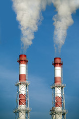 Two striped industrial pipes with smoke over cloudless blue sky