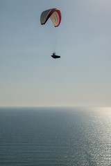 Lone paraglider flying high over the ocean
