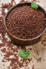 Close-up of a wooden bowl with raw red rice, studio shot