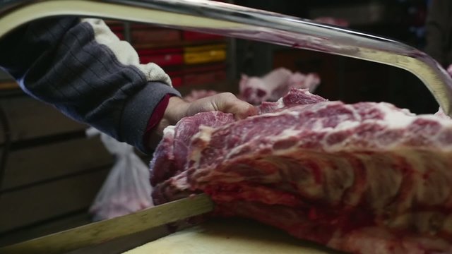 Old butcher cutting pig meat with saw in slow motion
