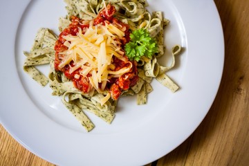 Green herb pasta with bolognese sauce on white plate, close view