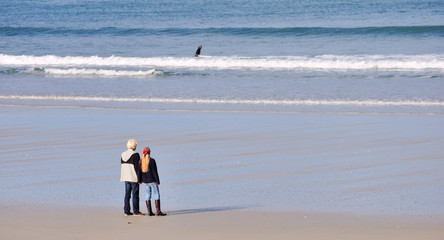 Couple se tenant la main qui regarde des surfeurs sur une plage