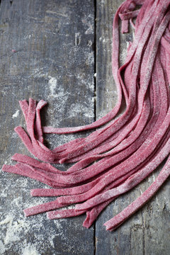 homemade pasta tagliatelle with beetroot on table with flour