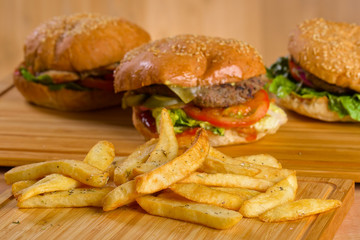 Tasty burger with melted cheese and thick succulent ground beef patty, lettuce, tomato, onion, sesame bun standing on wooden table