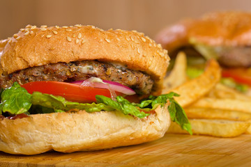 Tasty burger with melted cheese and thick succulent ground beef patty, lettuce, tomato, onion, sesame bun standing on wooden table