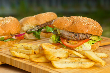 Tasty burger with melted cheese and thick succulent ground beef patty, lettuce, tomato, onion, sesame bun standing on wooden table