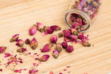 Dried roses, wooden scoop of rose tea on bamboo mat