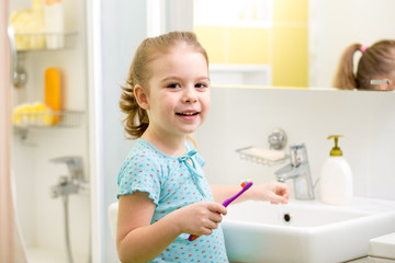 Smiling child brushing teeth in bathroom
