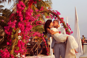 Bride and groom embracing near arch of flowers in Maldives