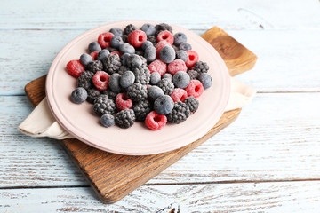 Iced berries on plate, on color wooden background