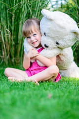 Little elfin girl sittinging in the grass with large teddy bear