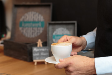 Männerhand hält Kaffee in Tasse vor Tresen Kulisse