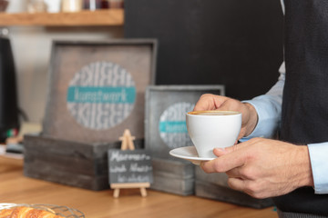 Männerhand hält Kaffee in Tasse vor Tresen Kulisse