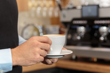 Männerhand hält Kaffee in Tasse vor Kaffee Maschine als Kulisse