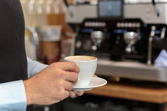 Männerhand hält Kaffee in Tasse vor Kaffee Maschine als Kulisse