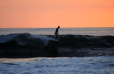ein Surfer surft die letzte welle vor roter Abendsonne