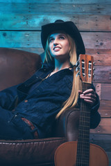 Cowgirl country singer with acoustic guitar. Sitting on leather