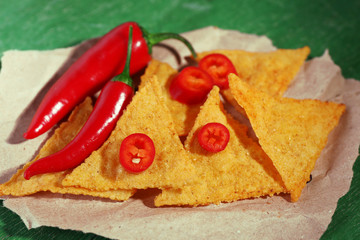 Tasty nachos and chili pepper on paper, on wooden background