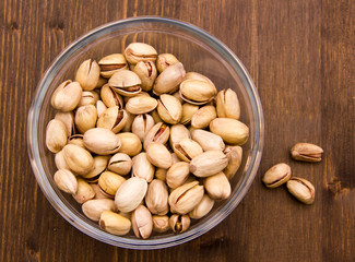 Pistachios on glass bowl on wooden table seen from above