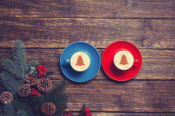 Two cups with christmas tree shape near branch on a wooden table