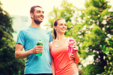 Obraz premium smiling couple with bottles of water outdoors