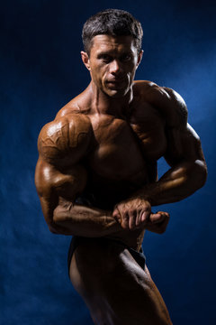 Handsome muscular bodybuilder posing over blue background