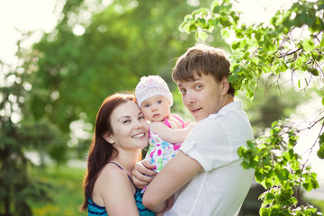 Portrait of young family with baby daughter in summer park