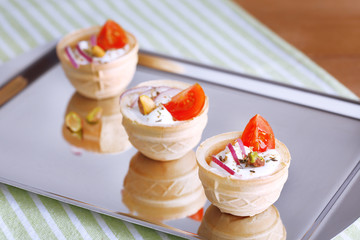 Tartlets with greens and vegetables with sauce on tray on table