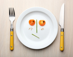 Vegetable face on plate with knife and fork on wooden table