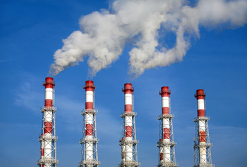 Five industrial pipes with white smoke over blue sky