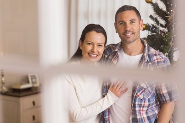 Fototapeta premium Smiling couple cuddling near the christmas tree