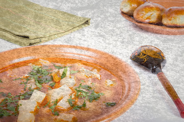 plate of vegetable soup, a wooden spoon and cakes on a light bac