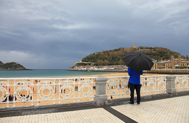san sebastián donostia hombre con paraguas mirando a la playa de la concha desde la barandilla...