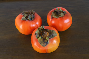 Three ripe persimmon on the wooden background