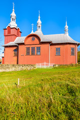 Red wooden church on green meadow in Czyrna village, Poland