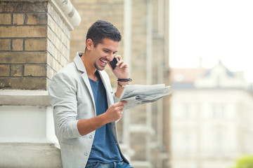 Young businessman reading newspaper and talking on the phone