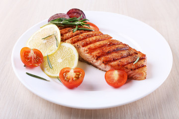 Grilled salmon and vegetables on plate on wooden background