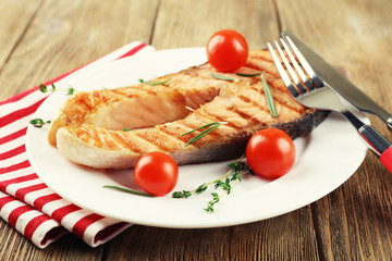 Grilled salmon and vegetables on plate on wooden background